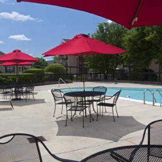 A sunny outdoor pool area with tables, chairs, and red umbrellas.