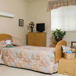 A cozy single bedroom with floral decor, featuring a dresser, TV, and a large window.