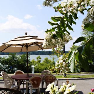 A serene outdoor patio with a view of the lake, featuring chairs and an umbrella under a clear summer sky.