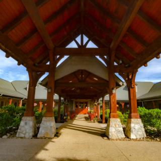A wooden covered walkway leading to a building entrance, surrounded by greenery.