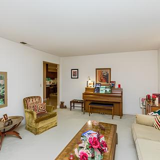 A retro-style living room featuring a piano, armchair, sofa, and coffee table with floral decor.