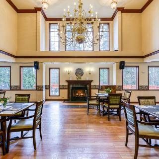 A spacious dining room with elegant decor, featuring a chandelier, fireplace, and multiple tables with chairs.