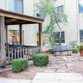 A peaceful courtyard with a covered seating area, surrounded by plants and a stone pathway.
