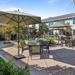 An inviting outdoor patio with tables, chairs, and umbrellas surrounded by a garden setting.