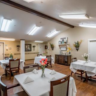 An elegantly decorated dining room with neatly arranged tables and chairs, featuring floral centerpieces.