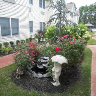 A small, landscaped garden with blooming flowers, a decorative pond, and a statue alongside a pathway.