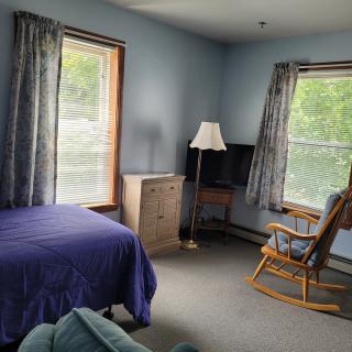 A cozy bedroom with a bed, rocking chair, TV, and large windows letting in natural light.