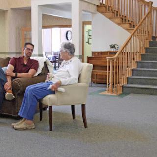 A relaxed conversation between two individuals in a cozy living room with a staircase in the background.
