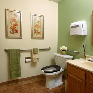 A clean and neatly arranged bathroom with green walls, decorated with floral artwork and equipped with essential amenities.