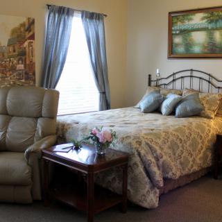 A cozy bedroom with a bed, recliner, and side table under soft lighting.