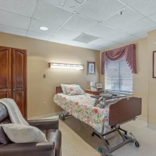 A cozy hospital room with a bed, comfortable chair, and window with drapes.