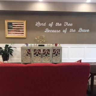 A memorial space featuring an American flag and a patriotic quote on the wall: 'Land of the Free, Because of the Brave.'