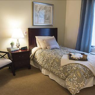 A cozy bedroom with a single bed, a bedside lamp, and a chair.