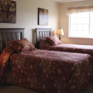 A cozy bedroom with twin beds adorned with floral bedding, a window letting in natural light, and a bedside lamp for evening ambiance.