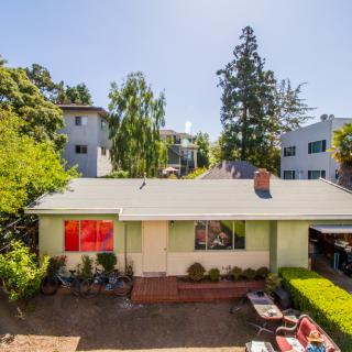 A suburban house with a yard, surrounded by trees under a sunny sky.
