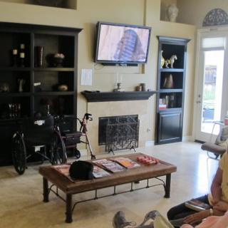 A cozy living room with a television above the fireplace, surrounded by shelves and a bicycle leaned against the wall.
