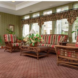 A cozy living room featuring a rattan sofa set with colorful cushions, a wooden coffee table, and large windows adorned with patterned curtains.