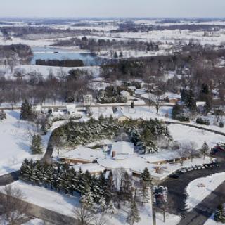 A serene winter landscape blanketed in snow, showcasing an aerial view of a rural area with winding roads and a river.