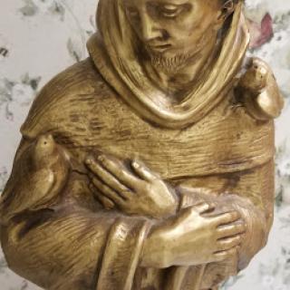 A beautifully crafted golden statue of a monk holding birds.