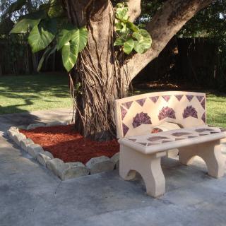A decorative bench under the shade of a large tree in a well-maintained garden.