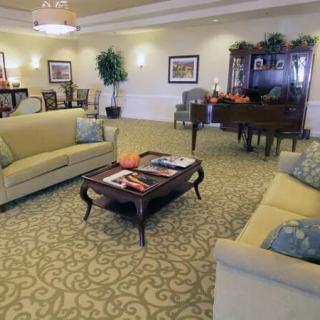 A cozy living room featuring sofas, a coffee table with magazines, and a piano in the background.