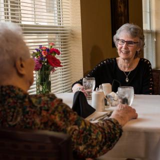 Two elderly individuals enjoying a conversation over a meal at a dining table.