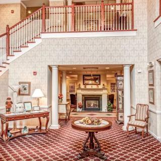 A warmly decorated lobby area featuring a fireplace, elegant furniture, and a staircase with red railings.