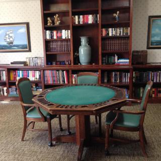 A cozy library room with a green card table surrounded by chairs and filled bookshelves.