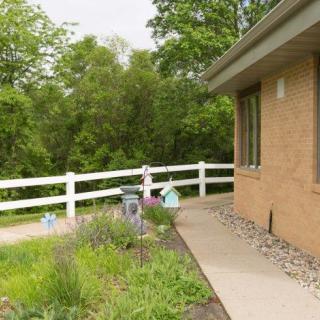 A house with a garden and white fence along a sidewalk, surrounded by greenery.