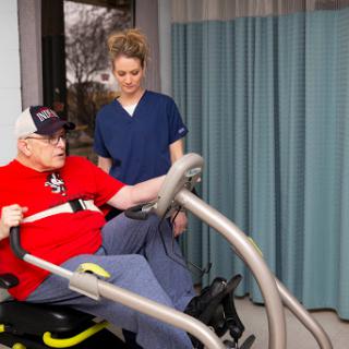 A healthcare professional assists an elderly patient with exercise equipment during a physical therapy session.