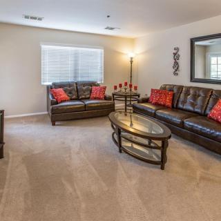 A cozy living room with leather sofas, red throw pillows, a glass coffee table, and a standing lamp.