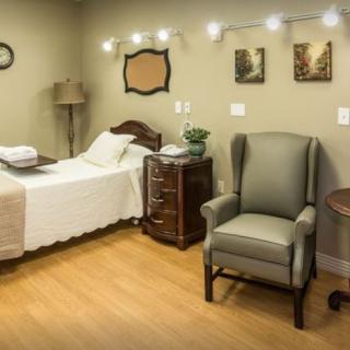 A cozy bedroom with a bed, armchair, and nightstand, accented by warm lighting and wall decor.