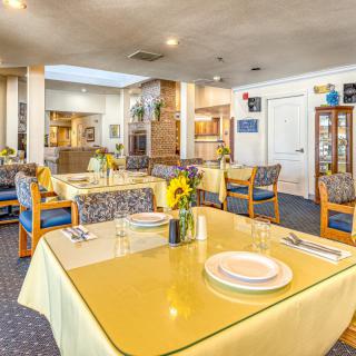 A bright dining area with tables set for a meal, featuring yellow tablecloths and floral decorations.