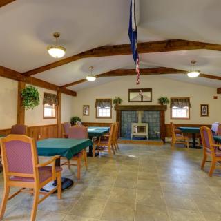 A spacious community room with tables and chairs, featuring a fireplace and a flag hanging from the ceiling.