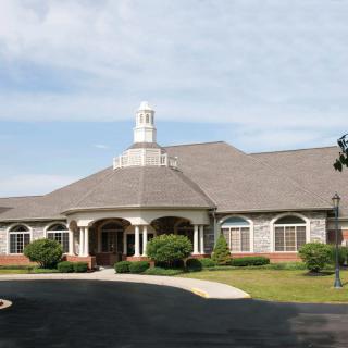 A large, elegant building with a central entrance and well-maintained landscaping under a cloudy sky.