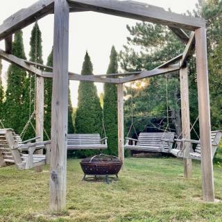 A backyard setup featuring a wooden swing structure surrounding a fire pit, offering a cozy seating area.