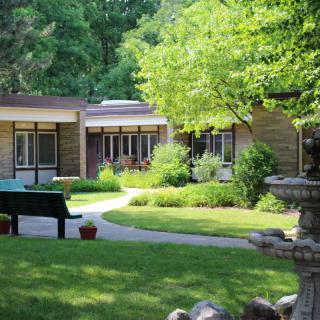 A tranquil garden setting with a fountain, surrounded by lush greenery and a modern building in the background.