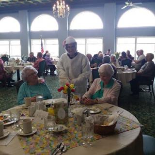 A chef serving two elderly women seated at a dining table in a restaurant setting.
