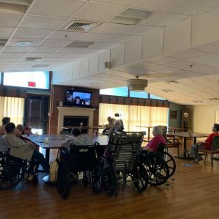 A group of seniors in wheelchairs watching television in a nursing home common area.