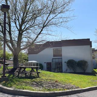 A serene outdoor view featuring a modest building surrounded by greenery and a picnic area.