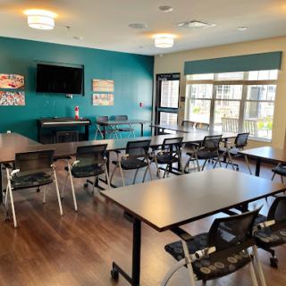 A well-lit meeting room equipped with tables, chairs, and a television for presentations.