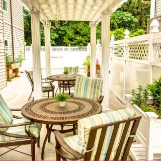 A cozy patio area with wooden tables and chairs beneath a pergola, surrounded by greenery.