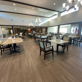 An empty dining area with neatly arranged tables and chairs, featuring chandeliers and a spacious layout.