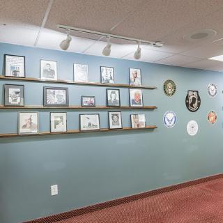 A wall display in an art gallery featuring a collection of framed pictures and decorative plates.