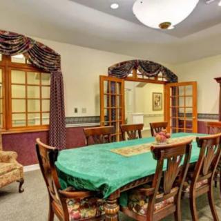 A well-furnished dining room featuring a long table with a green tablecloth, surrounded by wooden chairs, and adorned with elegant curtains and a chandelier.