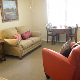 A cozy living room with a beige sofa, orange armchair, and a small dining table by the window.