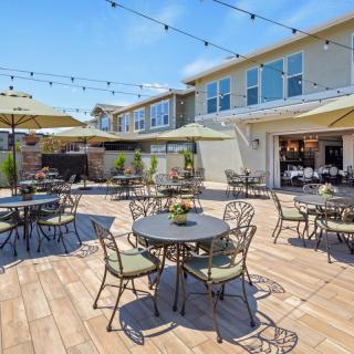 A sunny outdoor patio with tables, chairs, and umbrellas set under string lights.