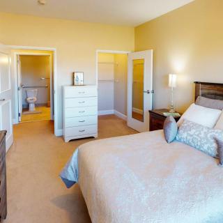 A cozy bedroom with neutral colors featuring a bed, dresser, and carpeted floor.