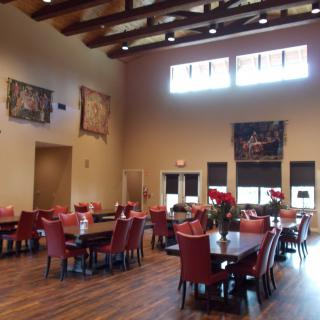 A spacious dining area with red chairs and wooden accents, illuminated by natural light from large windows.