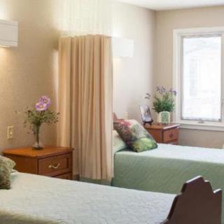 A cozy bedroom with twin beds, divided by a curtain, featuring nightstands and vases of flowers.